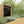 Load image into Gallery viewer, Wooden garden shed in a garden setting with a deck and flowers.
