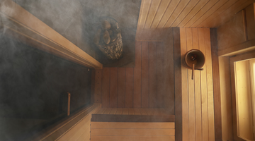 A wooden sauna room with warm, glowing wood panels. Steam is rising gently from a heated area, creating a cozy atmosphere.