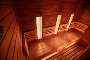 A modern infrared sauna with light wood benches. Infrared heating elements on the walls emit a soft glow, creating a calming, spa-like atmosphere.