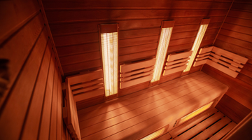 A modern infrared sauna with light wood benches. Infrared heating elements on the walls emit a soft glow, creating a calming, spa-like atmosphere.