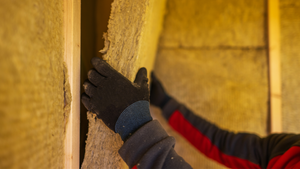 Worker with gloves installing insulation in the interior walls of a sauna to improve heat retention and energy efficiency