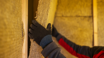 Worker with gloves installing insulation in the interior walls of a sauna to improve heat retention and energy efficiency