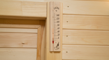 Thermometer displaying a temperature of 65 degrees celsius inside a wooden sauna. 