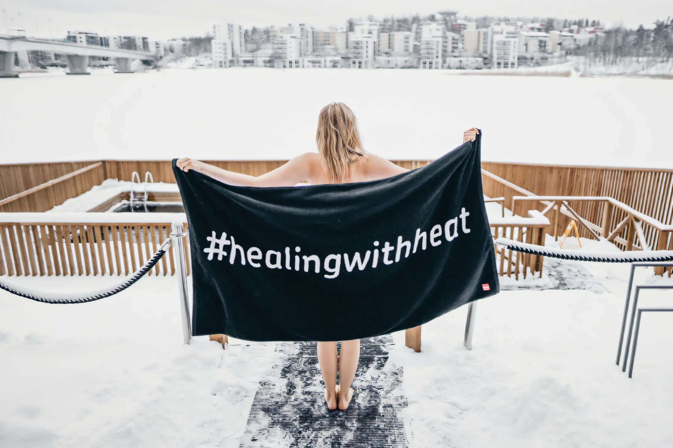 Person wrapped in a black towel with '#healingwithheat' text on a snowy rooftop.