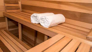 Wooden bench in a sauna with rolled towels on it