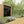 Wooden garden shed in a garden setting with a deck and flowers.